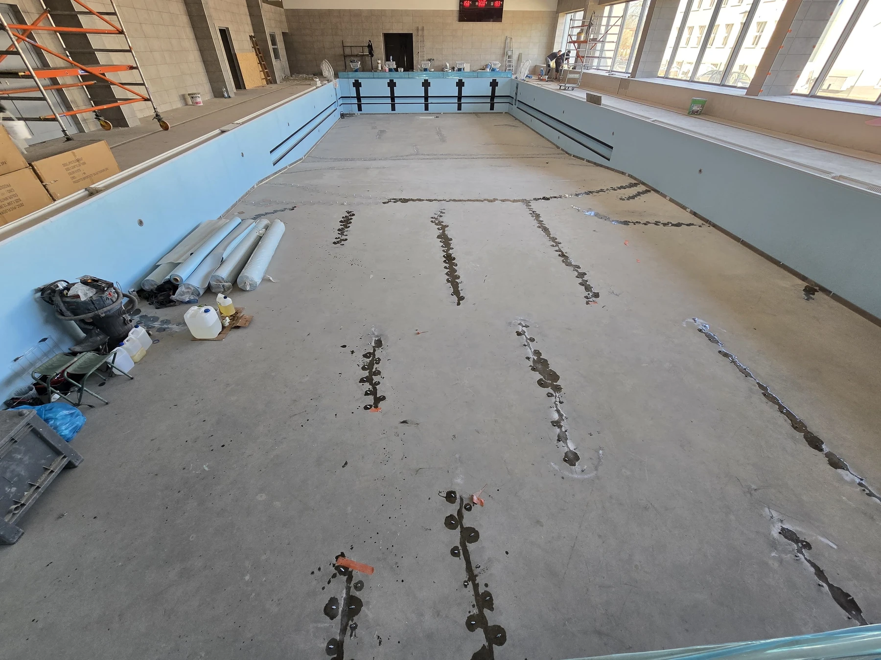 Tukšas baseina bļodas skats ar redzamām materiāla pēdām gar remontētajām plaisām betona dibenā.