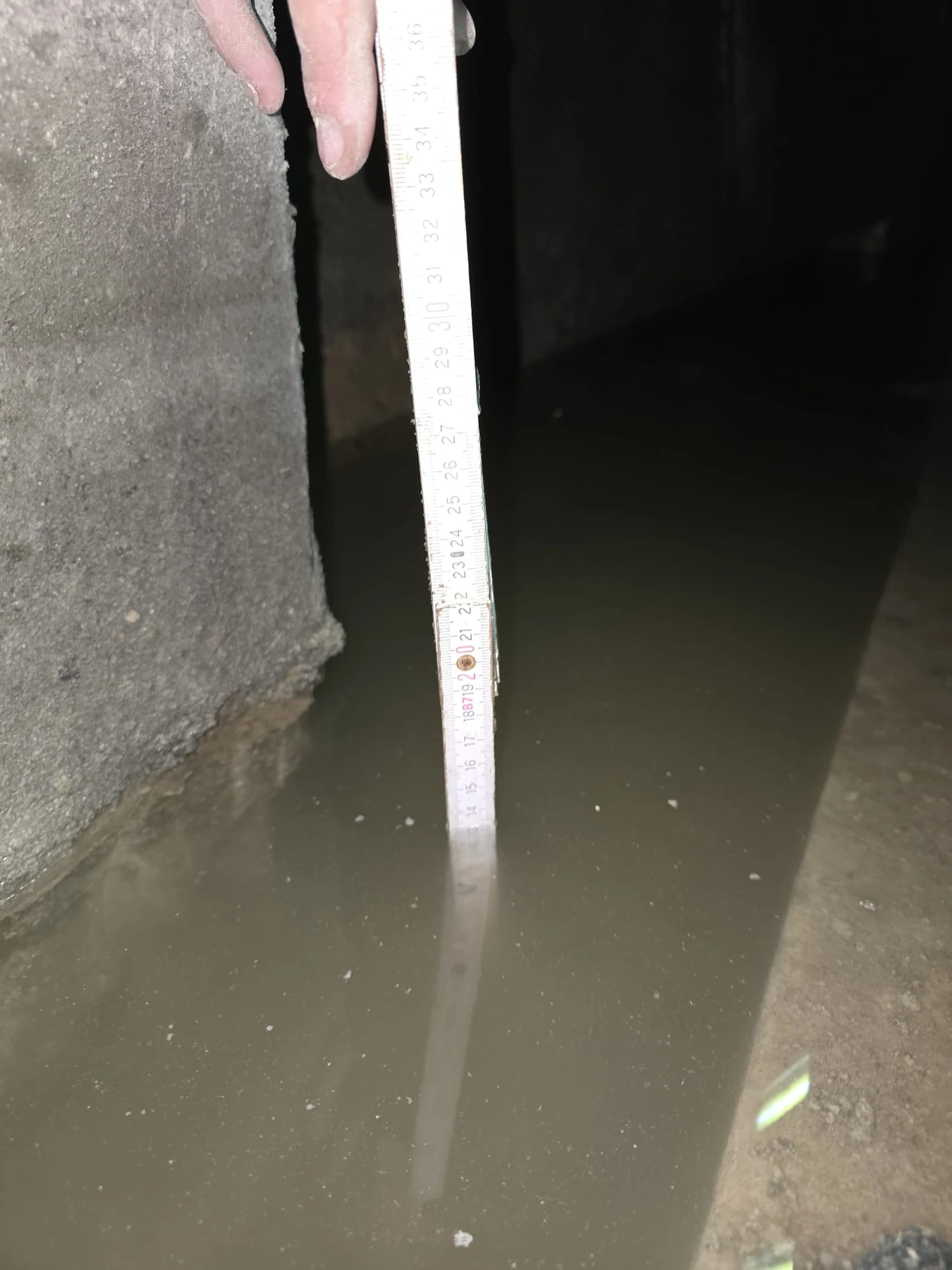 Apă acumulată lângă peretele subsolului și riglă poziționată vertical care arată nivelul inundării.